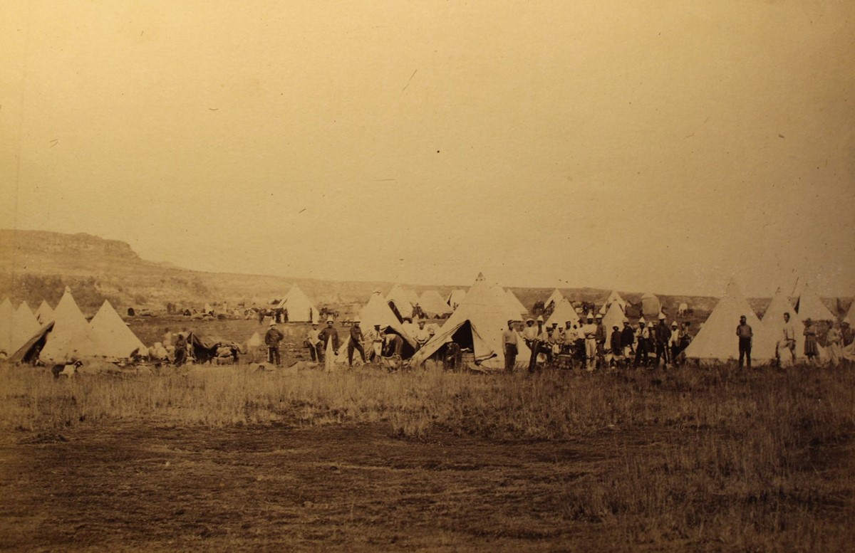 photo of soldiers standing around a group of white conical tents.