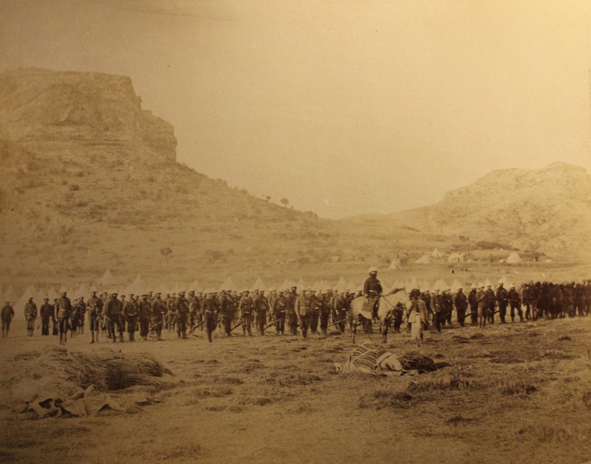 photo of military parade in front of tents at the foot of a rocky hill.