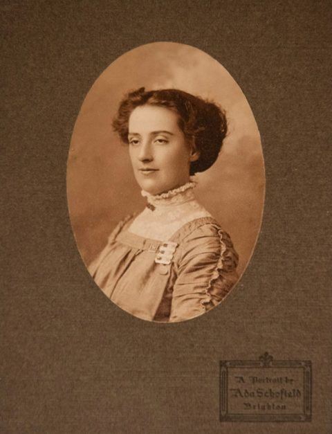 Photo of Selina Martin in an oval mount. She has dark curly hair put up in a formal style and wears a dark dress with a high collar in white lace. A stamp at the bottom right reads 'A portrait by Ada Schofield, Brighton'.