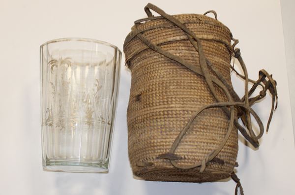 photo of a glass tumbler decorated with gold patterns beside a storage basket with a tightly fitted lid and leather carrying straps..